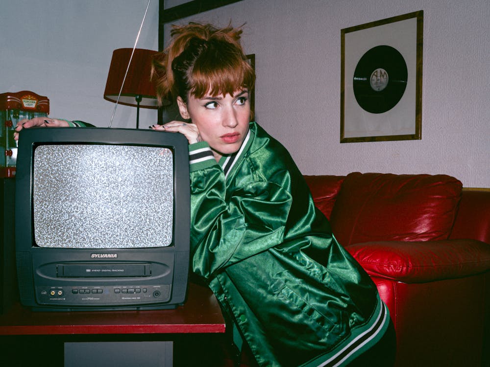 A woman in a green jacket is holding an old television