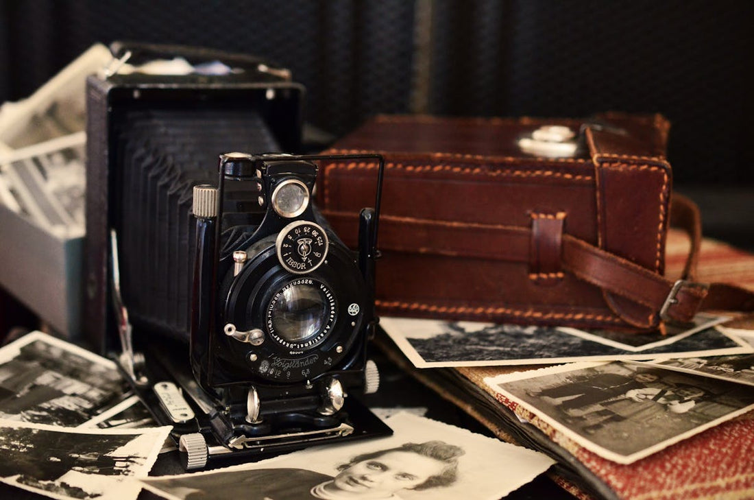 Black Folding Camera Beside Brown Bag on Grayscale Photos